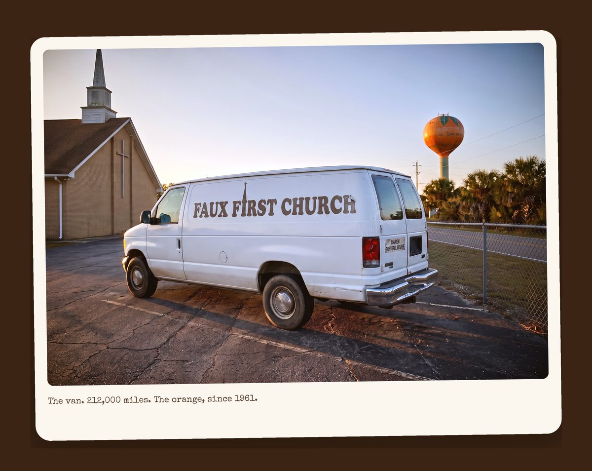 A white 1994 Ford E-350 fifteen-passenger van with FAUX FIRST CHURCH on its side, parked at sunset beside the church, with a water tower painted like an orange in the distance.
